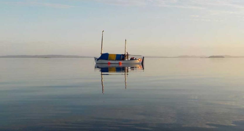 A sailboat floats on calm water, reflecting the gentle colors of the sky.